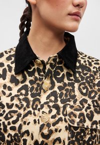 Leopárd mintás farmerdzseki fekete velúr gallérral, két gombos zárással, és texturált anyaggal, amelyen egy mellzseb található.