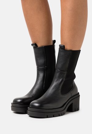 Stivaletti neri alla caviglia in pelle testurizzata con pannelli elastici ai lati e tacco spesso e robusto. Dotati di linguette per una facile calzata.