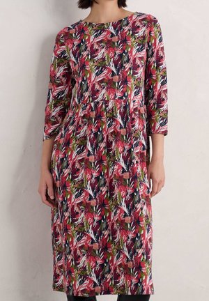 Woman wearing a knee-length dress with long sleeves and a multicolored floral pattern in red, green, navy, and white.