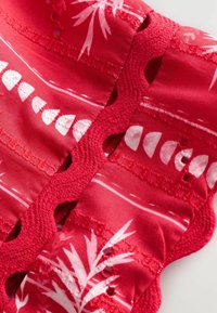 Tessuto rosso con motivi di foglie tropicali bianche, dettagliato con bordi scallop e accenti ritagliati. Texture liscia, materiale leggero.