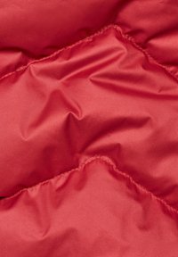 Tissu de veste rembourrée rouge avec une texture lisse et brillante. Présente un motif en losanges matelassé et des coutures visibles le long des coutures.