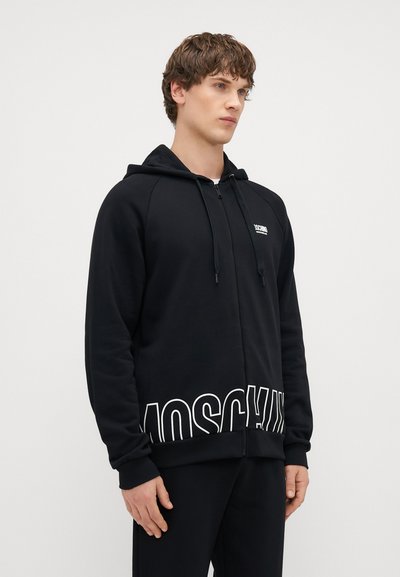 Fekete, cipzáros kapucnis felső pamut keverékből, fehér "Moschino" logóval az alján, állítható húzózsinórral a kapucnin és bordás mandzsettákkal és aljjal.