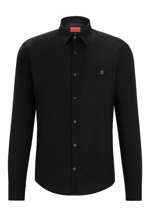 Camisa negra de manga larga con cuello clásico, cierre de botones, logo sutil en el pecho y una textura de tela suave.