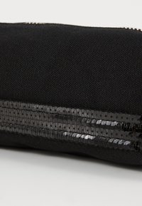 Svart stoffpung med en glinsende paljettstripe for ekstra tekstur. Glidelås lukking er synlig langs toppkanten.
