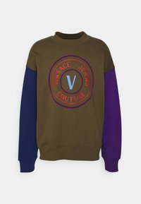 Olivgrön sweatshirt med lila och blå ärmar, med en cirkulär logotyp med röd text "VERSACE JEANS COUTURE" och ett centralt blått "V".