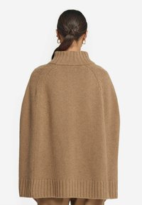 Tan stickad poncho med hög krage, ribbad nederkant och lös passform. Slät textur, enfärgad och raglanärmar definierade av subtila sömmar.