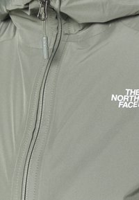 Hellgrüne Zip-Jacke mit glatter Oberfläche, ausgestattet mit einem weißen Logo, verstellbarem Kapuzenkragen und kontrastierenden schwarzen Nähten.