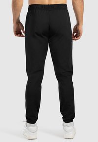 Zwarte sport joggers met een elastische tailleband en boorden bij de enkels. Gladde stof met minimale stiksels en geen zichtbare zakken.