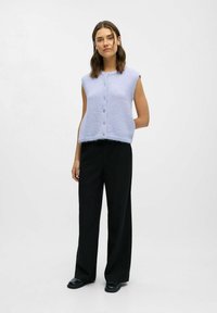 Lys lilla ærmeløs cardigan med rund hals, struktureret strik og fem knapper. Sættes sammen med blege sorte ternede wide-leg bukser og mørke sko.