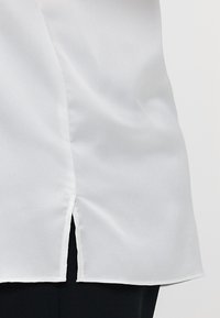 Blusa bianca con un tessuto liscio e leggermente testurizzato. Presenta un'apertura laterale all'orlo e una vestibilità comoda.