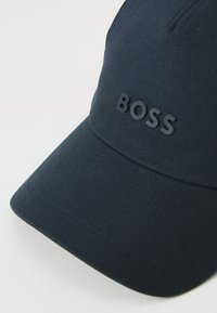 Sötétkék sapka texturált anyagból, lapos axával és gumi „BOSS” logóval az elején.