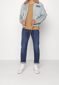 Světle modrá bomber bunda s béžovým límcem z umělé kožešiny; hnědý tričko; tmavě modré džíny; bílé tenisky; stříbrný zip a černý štítek jako detaily.