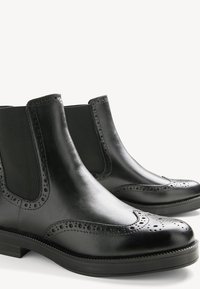 Black leather Chelsea boots with a smooth finish, decorative brogue detailing, elastic side panels, and a low block heel.