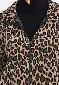 Kurtka polarowa w leopardzie wzory z czarnym zamkiem błyskawicznym i kołnierzem, o miękkiej, teksturowanej powierzchni w jasnobrązowych i ciemnobrązowych odcieniach.