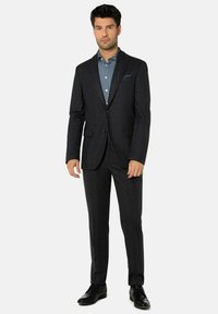 Dunkler maßgeschneiderter Anzug mit strukturierter Oberfläche, ausgestattet mit einem Ein-Knopf-Sakko, Revers mit Kerbe und schlanken Hosen. Kombiniert mit einem hellblauen Hemd.