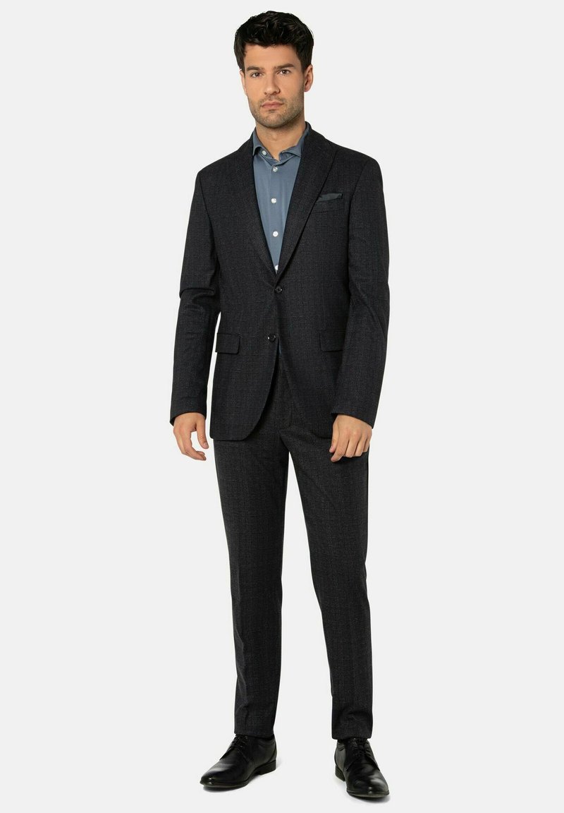 Dunkler maßgeschneiderter Anzug mit strukturierter Oberfläche, ausgestattet mit einem Ein-Knopf-Sakko, Revers mit Kerbe und schlanken Hosen. Kombiniert mit einem hellblauen Hemd.
