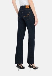 Jeans in denim blu scuro con design a gamba dritta, dotati di etichetta in pelle marrone sulla vita e cuciture gialle sulle tasche posteriori.