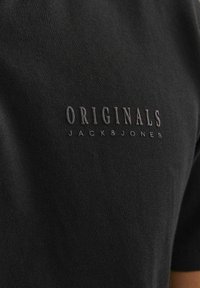 Mustat puuvillapaitat, joissa on tummalla langalla brodeerattu "ORIGINALS JACK & JONES", lyhyet hihat ja sileä pinta.