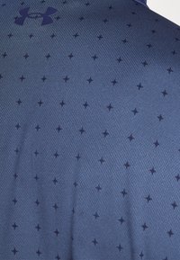 T-shirt de sport bleu marine en tissu texturé, présentant un motif de petites étoiles sombres et un logo contrastant sur la poitrine.