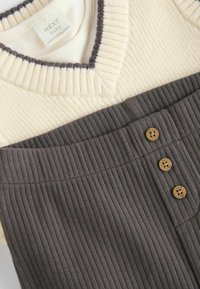 Creme- und graues, vertikal geripptes Kleid mit V-Ausschnitt, ausgestattet mit Holzknöpfen und kontrastierenden Texturabschnitten an Ober- und Unterseite.