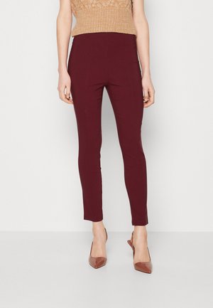 Pantaloni elasticizzati bordeaux con vita alta, aderenti e dalla texture morbida. Indossati con un top lavorato a maglia beige e tacchi a punta marroni.