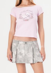 Rosa kortärmad t-shirt med grafik med texten "Unbothered" och blommönster, i kombination med en grå veckad kjol med lövdesign.