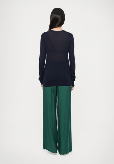 Tumesinise varrukateta särk, millel on keha järgnev lõige ja pehme tekstuur. Sobitatud laia lõikega roheliste pükstega, luues kontrastse silueti.