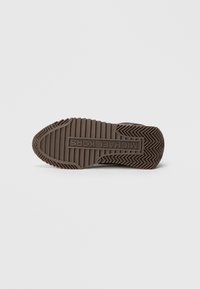 Suela de zapato de goma marrón con un dibujo en relieve y un logotipo rectangular grabado en el centro. Texturizada para proporcionar tracción con surcos.