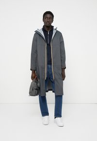 Hallgray veekindel jakk koos kapuutsi ja kollaste detailidega, paired with navy sinine tõmbluku-sveter ja sinised teksad. Valged tossud lõpetavad välimuse.