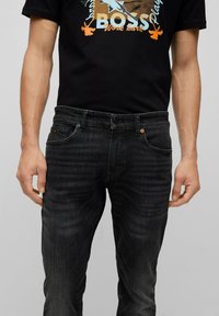 Jeans in denim nero con una vestibilità slim, dotati di tasche frontali, chiusura con bottone e zip, e leggeri sbiadimenti lungo le gambe.