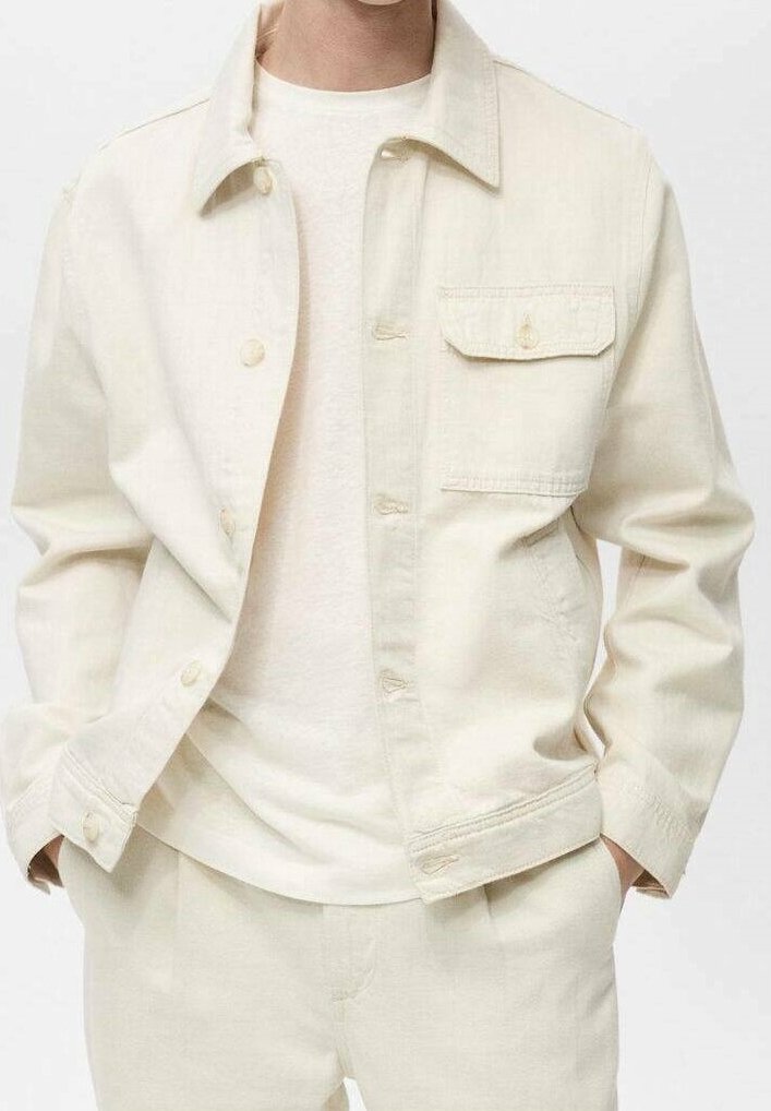 Giubbotto di jeans beige chiaro con bottone frontale, tasca sul petto singola e colletto classico; indossato sopra una maglietta leggera e semplice. Texture liscia.