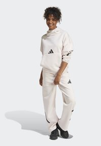 Light pink hoodie and pants set made from soft fabric, featuring black Adidas logo accents, relaxed fit, and elastic cuffs and waistband.