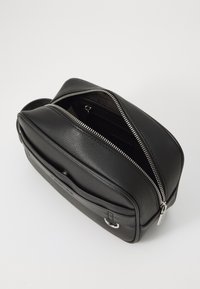 Bolsa crossbody de couro preto com acabamento texturizado, apresentando dois compartimentos com fechos zip e detalhes metálicos prateados.