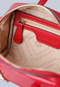 Bordeaux leren handtas interieur met een beige voering met een herhalend logo patroon, ritsvak en compact ontwerp. Gouden rits langs de rand.