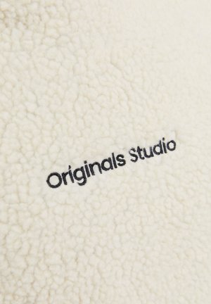White textured fleece fabric featuring black embroidery of the words "Originals Studio" on the surface.