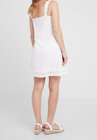 Vit klänning med spetsöverdrag, fyrkantig rygg och breda axelband. Kombineras med vita espadriller med justerbart vristband.