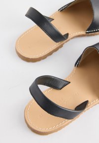 Sandales à semelle couleur fauve avec des brides en cuir noir croisées sur le dessus et des semelles extérieures en caoutchouc brun rainurées.