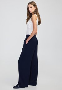 Szerokie, granatowe spodnie wykonane z lekkiego materiału, z wysokim stanem i bocznymi kieszeniami, zestawione z dopasowaną białą bluzką.