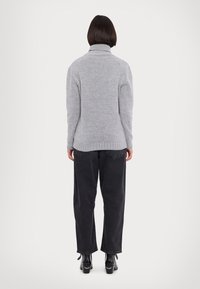 Pull tricot gris avec un col montant, poignets et ourlet côtelés ; porté avec un pantalon large noir et des bottes à talons noires.