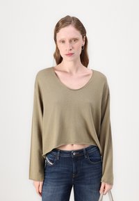 Top de manga larga recortado en verde oliva, confeccionado con una tela de punto suave, combinado con jeans ajustados de color azul oscuro. Textura suave y escote redondeado.