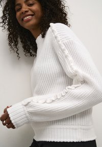Maglione bianco lavorato a maglia con polsi e orlo a coste, corpo testurizzato e dettagli arricciati lungo le maniche per un tocco in più.