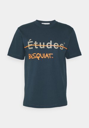 Tumma sininen lyhythihainen t-paita, jossa harmaalla "Études" -teksti ja sen yli menee oranssi viiva, ja alla oranssilla käsinkirjoitettu "BASQUIAT".