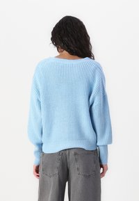 Lichtblauwe gebreide trui met een losse, oversized pasvorm, geribbelde textuur, wijde mouwen en een bootnek, gecombineerd met grijze high-waisted jeans.