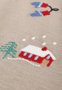 Tissu en maille crème avec un motif saisonnier brodé comprenant une maison rouge, un arbre vert, des flocons de neige et des moufles bleues en points détaillés.