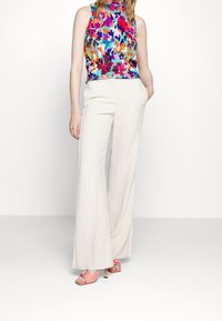 Top sin mangas de flores con textura acanalada en colores mixtos, combinado con pantalones de pierna ancha color crema y sandalias de tacón rosa, presentado sobre un fondo blanco.