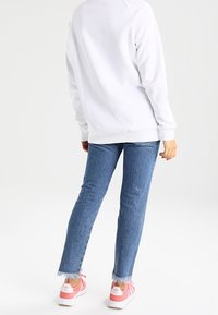 Valkoinen collegepaita, jossa on ribbireunat, yhdistettynä sinisiin farkkuihin, joiden helmassa on repaleiset yksityiskohdat, ja vaaleanpunaisiin lenkkareihin, joissa on valkoiset raidat ja logo.