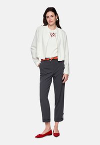 Weißes, kurzes Jackett, weißes Oberteil mit rotem Gürtel und Rautenmuster, graue, maßgeschneiderte Hose und rote Ballerinas mit Schleifendetail.