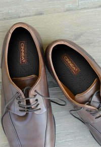 Brown leather shoes with rounded toes, decorative stitching, and laces. Textured black insole marked with "CINNEA."