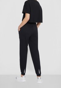 Zwart cropped t-shirt met korte mouwen, gecombineerd met zwarte joggingbroek met zijzakken en reflecterende accenten bij de manchetten.