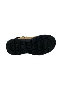 Shoe sole, black rubber with deep treads. Upper is tan, made of textured material, featuring a strap and buckle for secure fit.